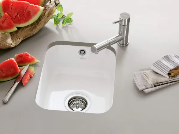 Cisterna sink in a grey worktop A sliced watermelon and a newspaper lie next to a white Cisterna undermount sink in a grey worktop