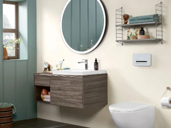 Baño de estilo rústico con la colección Subway 3.0 de Villeroy & Boch Moderno cuarto de baño con espejo redondo, tocador Villeroy & Boch Subway 3.0 montado en la pared, inodoro, toallero con artículos de tocador y ventana.