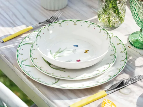 Frühlingshaft gedeckter Tisch mit Colourful Spring Tellern Ein gedeckter Tisch im Freien mit einem Colourful Spring Tablesetting und grünen Boston Gläsern unter natürlichem Licht.