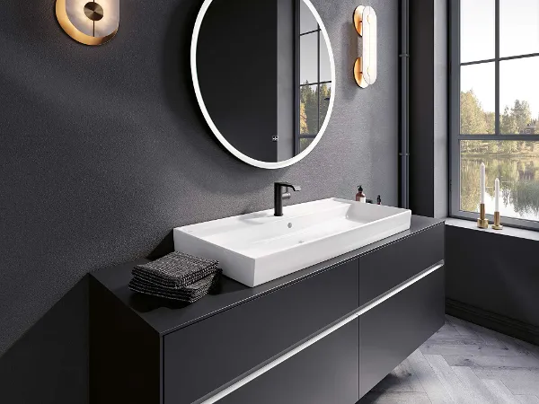 Une salle de bains moderne avec un lavabo blanc Collaro et des meubles de salle de bains Subway 3.0 de Villeroy & Boch. Une salle de bains moderne avec un élégant lavabo noir, une vasque blanche Collaro de Villeroy & Boch, un miroir rond rétroéclairé et des luminaires fixés au mur. Une grande fenêtre permet de bénéficier de la lumière naturelle et d’une vue sur l’extérieur.