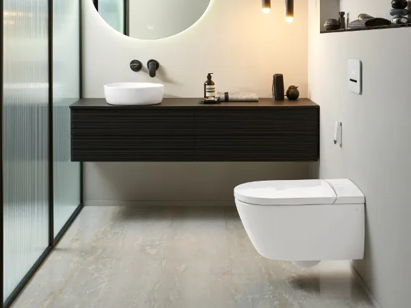Łazienka z kolekcji Antao z toaletą myjącą ViClean firmy Villeroy & Boch Nowoczesna łazienka z wiszącą miską WC, czarną szafką wiszącą z białą umywalką, podświetlanym okrągłym lustrem, lampami wiszącymi i ścianką działową z mlecznego szkła.