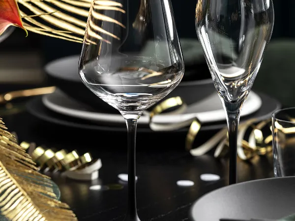Manufacture Weingläser elegant serviert Elegant gedeckter Esstisch mit zwei Villeroy & Boch Manufacture Weingläsern, schwarzen Tellern und goldenen Dekoelementen, darunter ein Farnblatt.