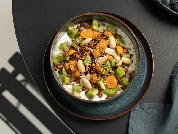 Crafted bowl on a plate filled with muesli A Crafted plate with a Crafted bowl filled with yoghurt, kiwi, muesli and apricots.