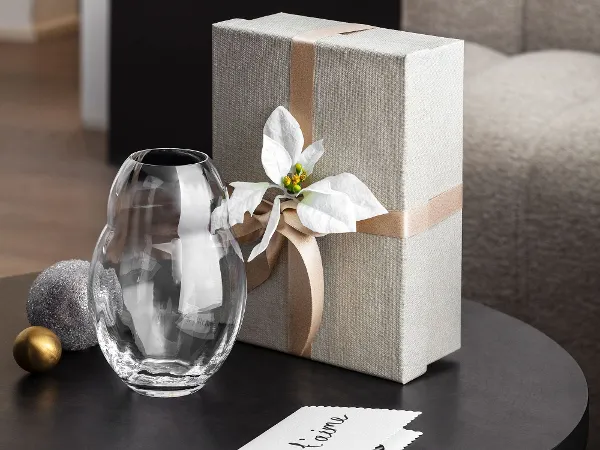 Ein Tisch mit einer verpackten Geschenkbox und einer dekorativen Rose Garden Home Glasvase Ein Tisch mit einer verpackten Geschenkbox, geschmückt mit einer weißen Schleife und einer dekorativen Rose Garden Home Glasvase
