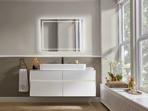 Modernes Badezimmer mit einem Villeroy & Boch Finion Waschbecken und einem Collaro Spiegel Modernes Badezimmer mit einem Villeroy & Boch Finion Waschbecken und einem Collaro Spiegel über einem weißen schwebenden Waschtisch, minimalistischem Dekor, einem Handtuchhalter und einem Fenster mit Blick ins Grüne draußen.