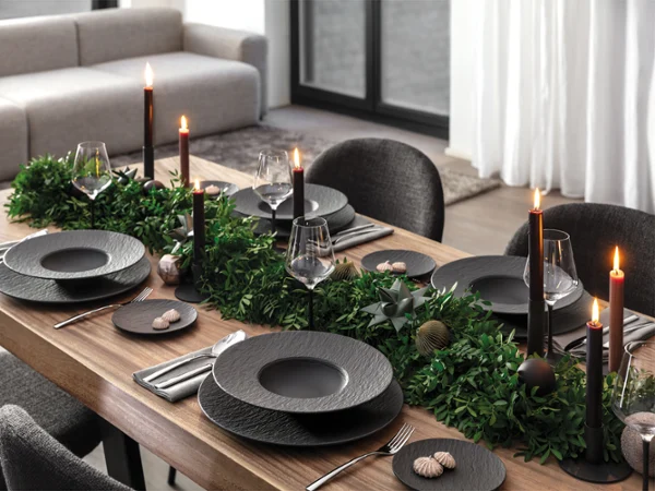 Elegant dining table set with black Manufacture plates Elegant dining table set with black Manufacture plates, black candles, cutlery and green foliage as a centrepiece in a modern dining room.