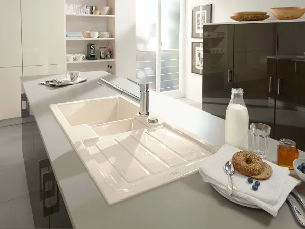 Un évier de cuisine Flavia avec des ingrédients pour le petit déjeuner Un plan de travail de cuisine moderne avec un évier Flavia beige, un robinet et des ingrédients pour le petit-déjeuner tels que du lait, des bagels et des myrtilles.