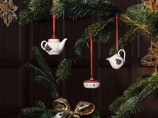 Toy‘s Delight Ornamente an einem Weihnachtsbaum hängen. Toy‘s Delight Ornamente, die mit roten Bändern und Stechpalmenmotiven an einem Weihnachtsbaum hängen.