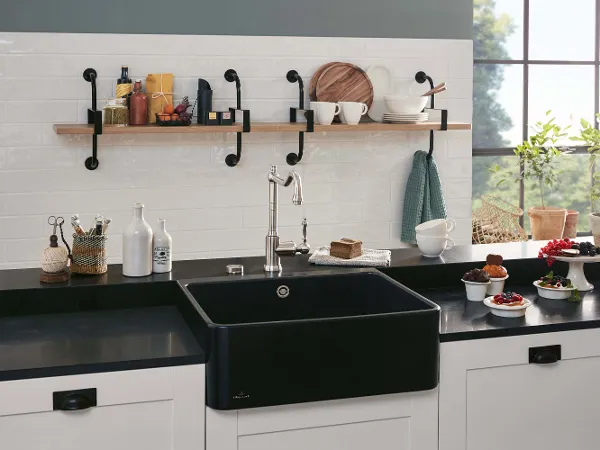 Black butler sink on a black worktop A black butler sink on a black worktop next to bowls and plates of fruit and muffins.