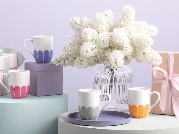 Vier Villeroy & Boch Fleur-Tassen Villeroy & Boch Fleur-Tassen in Pastellfarben, eine Fleur-Vase, Geschenkboxen und eine weiße Blumenvase auf sanft getönten Oberflächen.