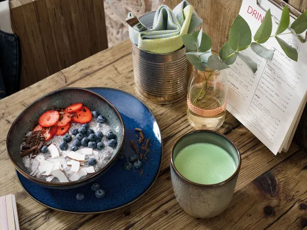 Lave Schüssel und ein Lave Becher Matcha Latte Eine gesunde Smoothie Bowl auf einem Holztisch in einer Lave Schüssel, einem Lave Becher Matcha Latte und einer Speisekarte.
