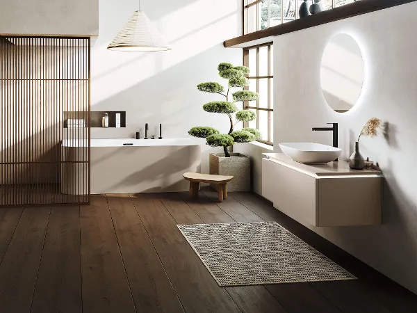 Une baignoire et un lavabo Loop & Friends dans une salle de bains de style japonais Une salle de bains minimaliste avec un sol en bois et de grandes fenêtres, une baignoire en îlot Loop & Friends, un lavabo Loop & Friends, un petit banc et un bonsaï en pot.