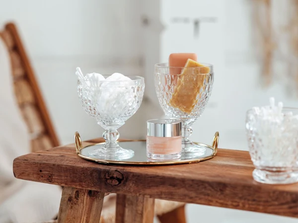 On a wooden stool there is a gold tray with two Boston glasses On a wooden stool there is a gold tray with two Boston glasses containing cotton wool and soap along with a small jar of cream.