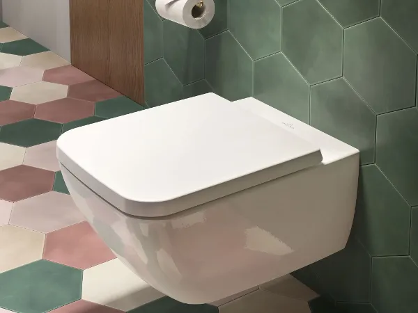 Venticello toilet with a toilet roll holder A modern bathroom with a Venticello toilet, hexagonal green tiles, colourful floor tiles, a wooden shelf and a toilet roll holder on the wall.