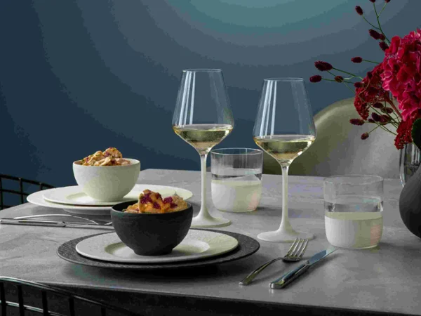 Manufacture black and white table setting with drinkware Elegant dining setup with two wine glasses, bowls of food, and a vibrant red flower arrangement on a gray table. The setting is calm and inviting.