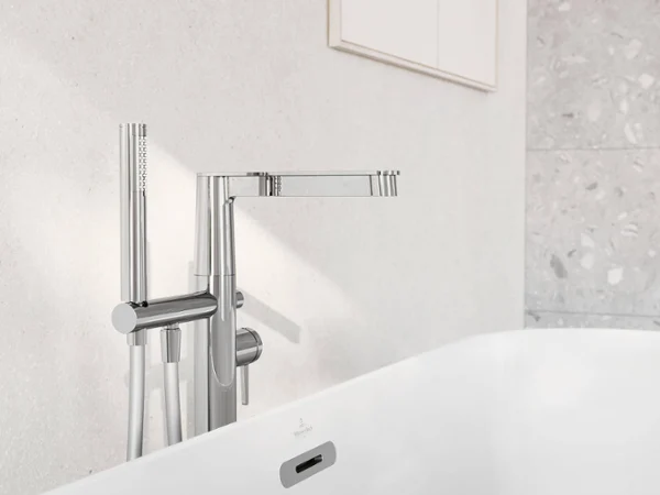 Conum bath tap with hand shower A modern chrome bath tap with a hand shower installed in front of a white tiled wall. The white bath is partially visible in the foreground.