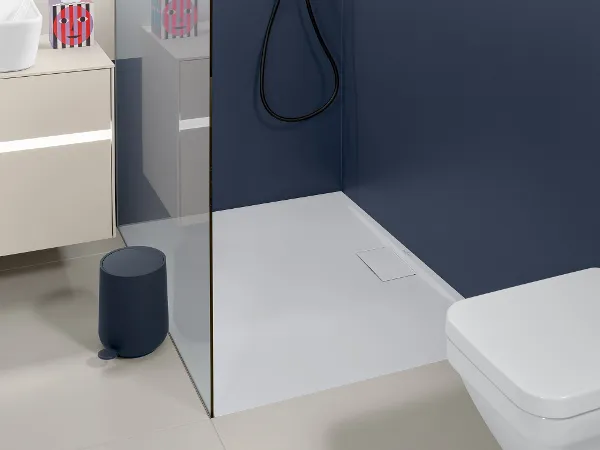 Une douche vitrée Architectura avec des parois bleues et une pomme de douche noir La salle de bains moderne dispose d’une douche vitrée avec une pomme de douche et une robinetterie noirs, de murs bleus et blancs, d’une niche murale avec des articles de toilette et de toilettes blanches. Il y a un lavabo et un tabouret.