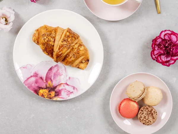Une composition de table élégante pour l’heure du thé avec un croissant, des macarons, une tasse de thé et des fleurs fraîches avec de la vaisselle Rose Garden sur une surface en marbre.