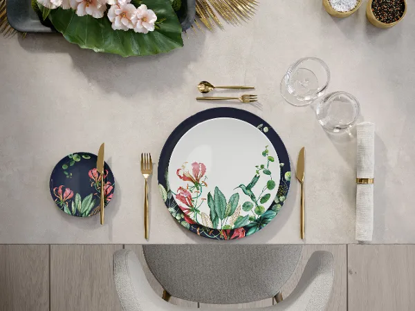 Table dressée avec une assiette Avarua et des couverts de table dorés MetroChic Un service de table avec de la vaisselle ornée de motifs floraux Avarua et des couverts de table dorés MetroChic.