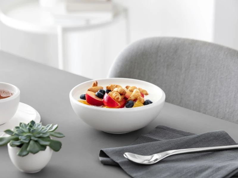 A healthy breakfast consisting of yogurt with mixed berries and cereal, served in a white NewMoon serving bowl.