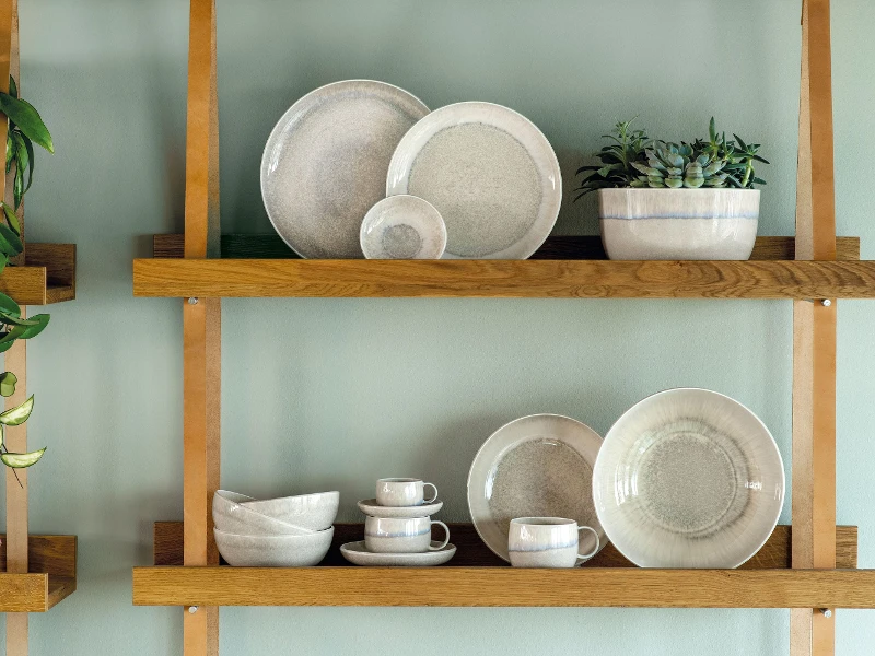 A wooden shelf with beige plates and bowls on it from the Perlemor collection.