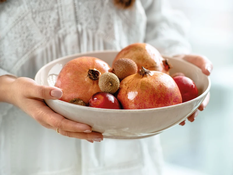 Een vrouw houdt een beige Perlemor kom met granaatappels en lychees in haar handen.