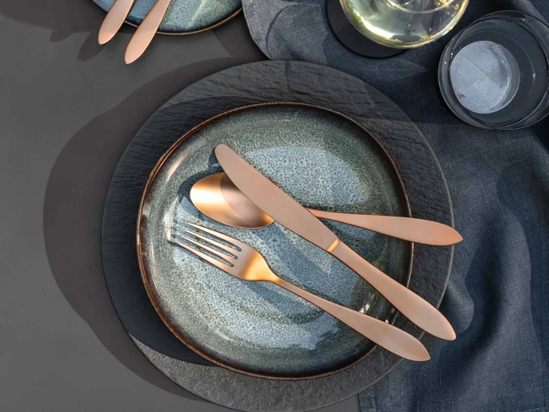 Elegant table decoration with two Lave plates, Manufacture cutlery, a bowl of olives and a glass of white wine on a grey tablecloth.