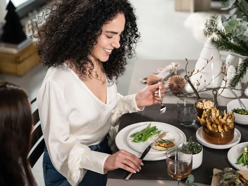 Woman in a white blouse smiling during dinner with a friend at a beautifully decorated table.