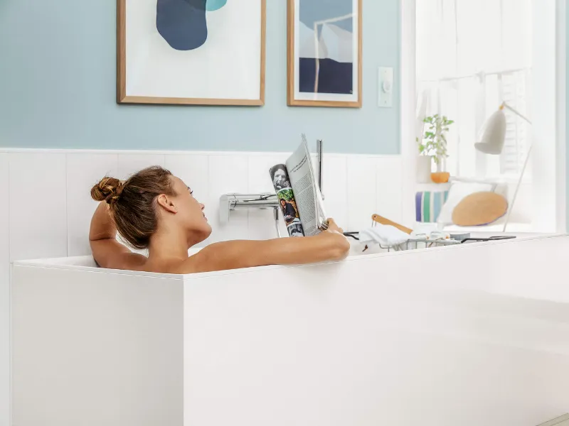 Une femme se détend dans une baignoire Subway 3.0 blanche en lisant un magazine.