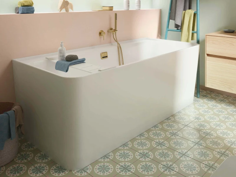 Salle de bain Collaro ludique avec baignoire blanche, robinetterie dorée et murs pastel. Les carreaux à motifs et les couleurs douces créent une atmosphère fraîche, lumineuse et invitante.