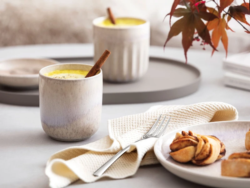 Ein Teller mit Gebäck und eine Tasse Kaffee in einem Perlemor Becher von like. by Villeroy & Boch auf einem Tisch.