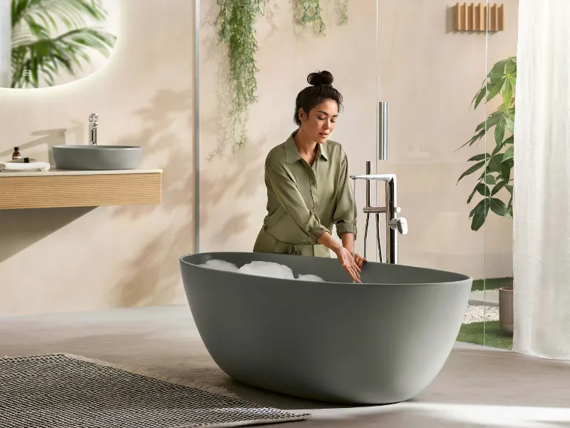 Una donna versa un bagno di schiuma in una vasca freestanding Antao verde.