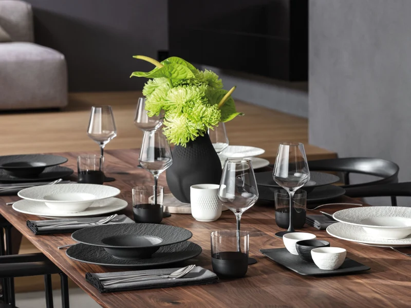 Une table élégamment dressée avec de la vaisselle de la collection Manufacture en noir et blanc, accompagnée d’un vase assorti.
