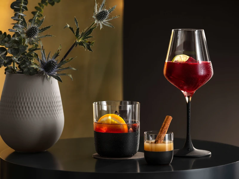 Deux cocktails servis dans des verres Manufacture et un vase Manufacture avec une plante sur une table noire devant un fond doré.