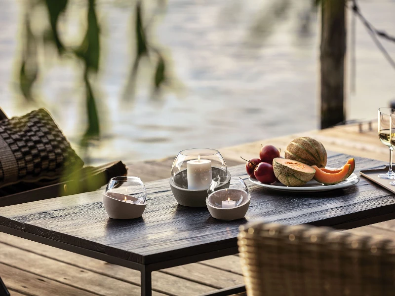 Des photophores NewMoon disposés sur une table en bois avec des fruits et du vin.