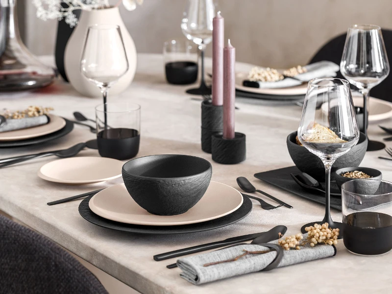 A table set with black Manufacture and beige NewMoon plates and black flatware.