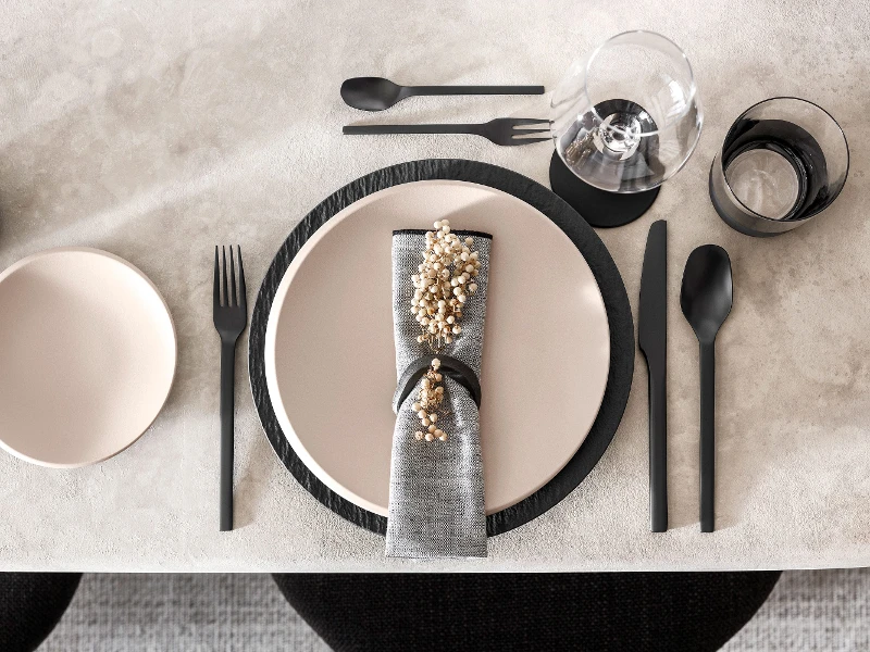 Une décoration de table moderne avec de la vaisselle NewMoon en beige et des couverts de table Manufacture noirs.