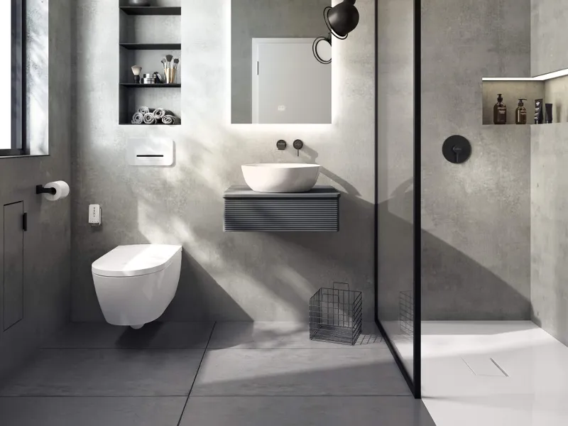 Moderne badkamer met betonnen muren, zwevend toilet, een ViClean douche-wc, wandwastafel, grote spiegel en glazen douche. Aan de muur hangen planken en toiletartikelen.