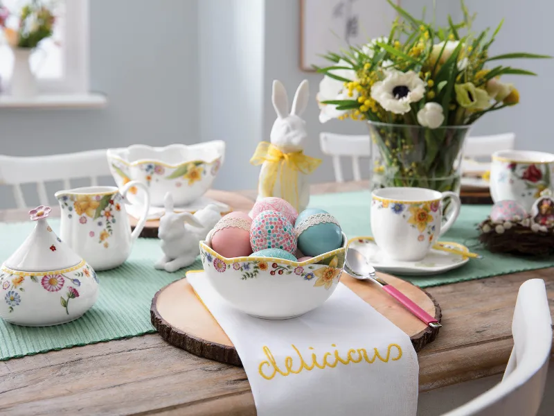 A colourful Easter brunch table set with floral tableware from the Spring Awakening collection with a bunny figurine and brightly painted eggs in a bowl.