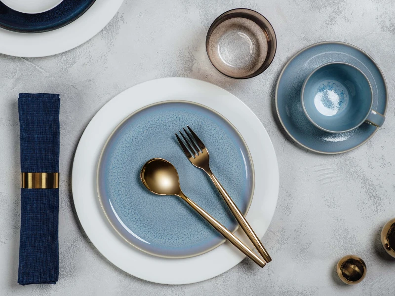 Elegant table decor with blue Crafted dinnerware and white Royal dinnerware, golden MetroChic flatware and a matching napkin.