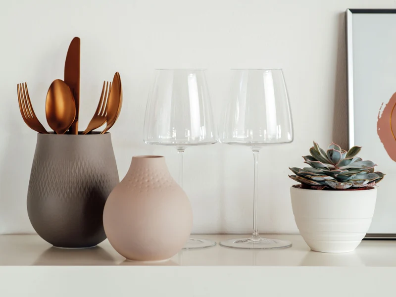 On a shelf, elegant golden cutlery is placed in one of two Manufacture vases, alongside two MetroChic wine glasses.