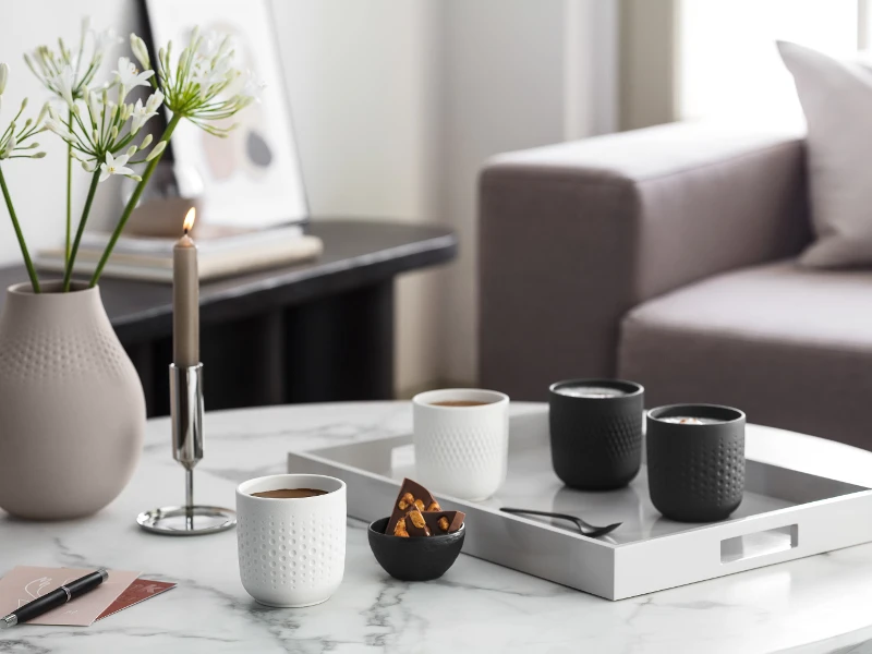 Elegant coffee table in the living room with Manufacture coffee mugs, candles, vases and a tray with cups and snacks.