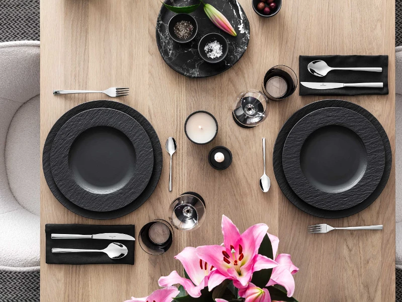 Modern table setting for two with black Manufacture dinnerware, Piemont flatware and pink lilies as the centerpiece.