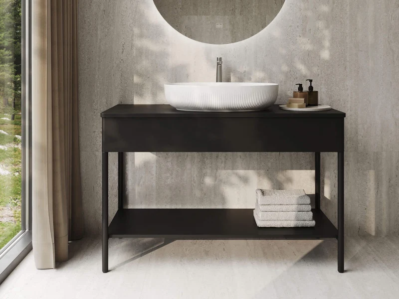 Baño moderno con un espejo redondo, un lavabo sobre encimera, un mueble de lavabo negro y toallas dobladas, situado junto a una gran ventana con cortinas.