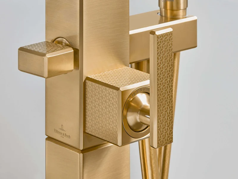 Close-up of a gold bath tap with a geometric pattern and two square buttons with a textured design.