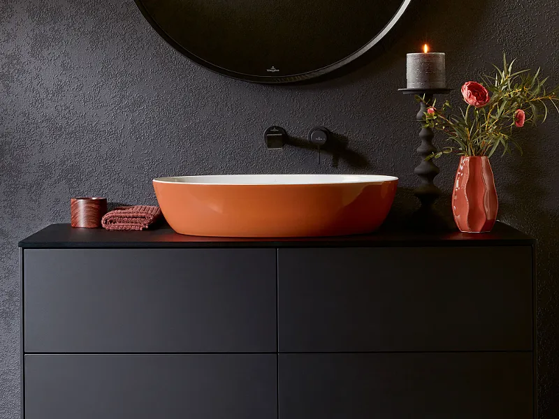 Interni di un bagno moderno con mobile Finion nero, lavabo Artis arancione intenso, specchio rotondo e luce geometrica