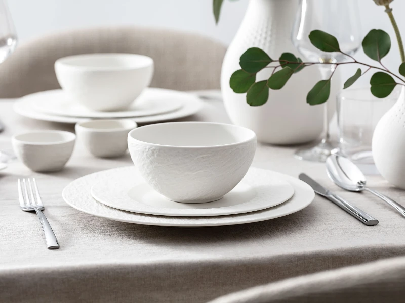 Elegant, wit servies uit de Manufacture collectie op een tafel met eenvoudige decoratie.