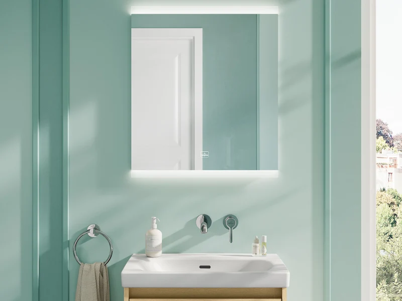 Fresh Modern Bathroom with Skyla Washbasin and More To See Square Mirror A bright, contemporary bathroom featuring a Villeroy & Boch Skyla washbasin with a light wood vanity unit, paired with a square More To See Square illuminated mirror. The space includes soft mint-green panelled walls, terrazzo flooring, wall-mounted fixtures, and minimalist accessories.