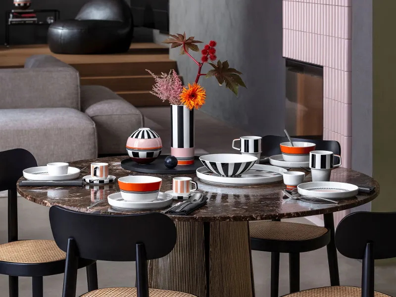 Dining table with black chairs, brightly patterned Memphis tableware, Memphis vases with flowers and contemporary decor in a modern space.