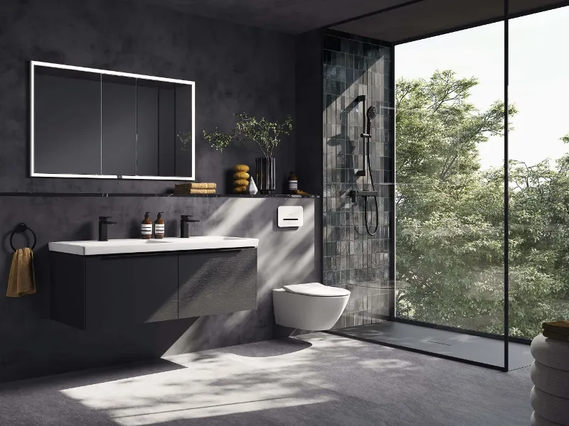 Modern bathroom with dark wall tiles, an illuminated square More to See Lite mirror, a black Loop & Friends surface-mounted washbasin on a floating Antao washstand and a towel holder with a pink towel, all in soft daylight.
